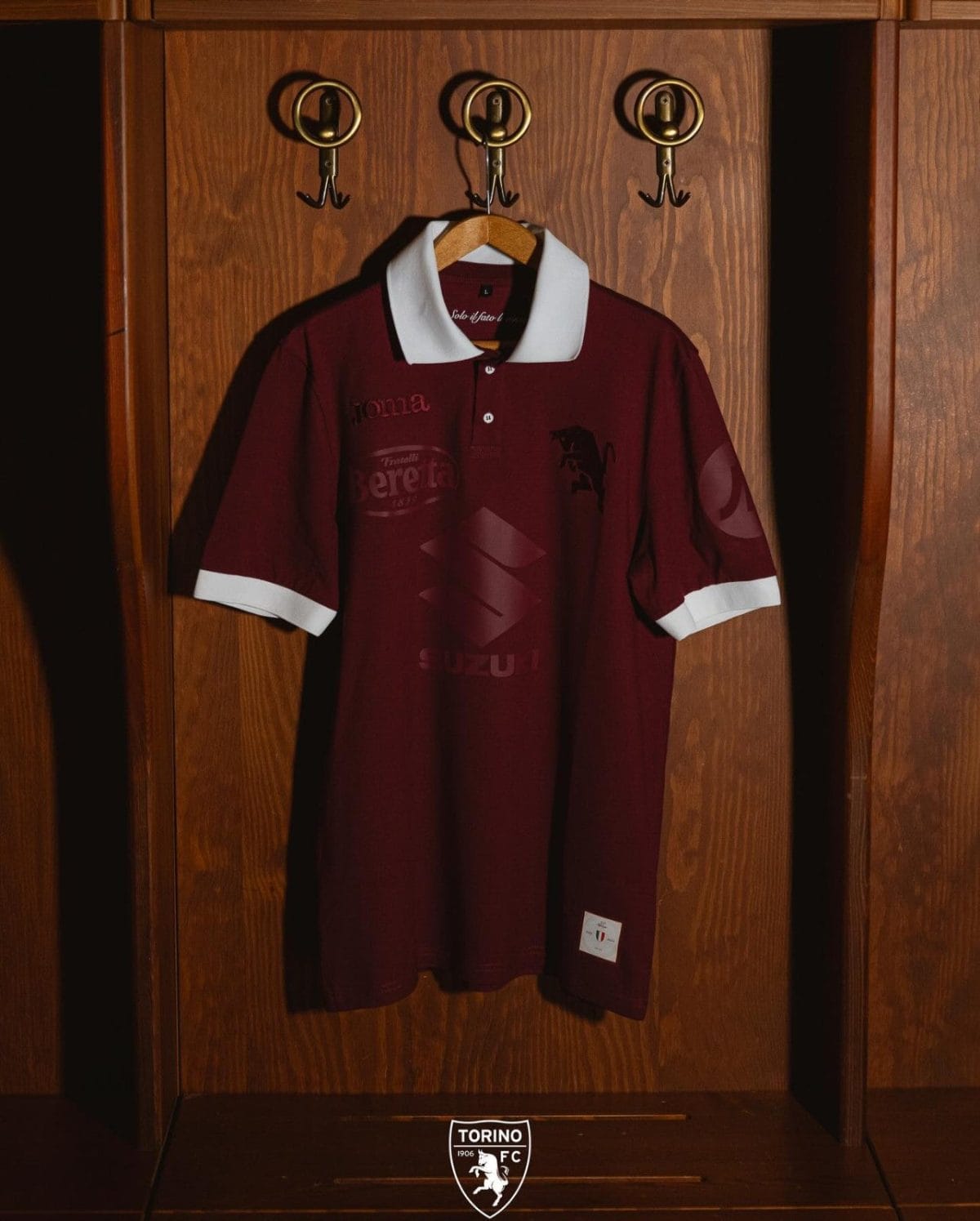 Maroon polo shirt with white collar hanging on a wooden wardrobe, Torino FC emblem visible at the bottom.