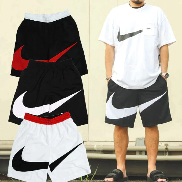 Man wearing a white Nike T-shirt standing beside black and white Nike shorts with oversized swoosh logos; multiple shorts are displayed nearby.
