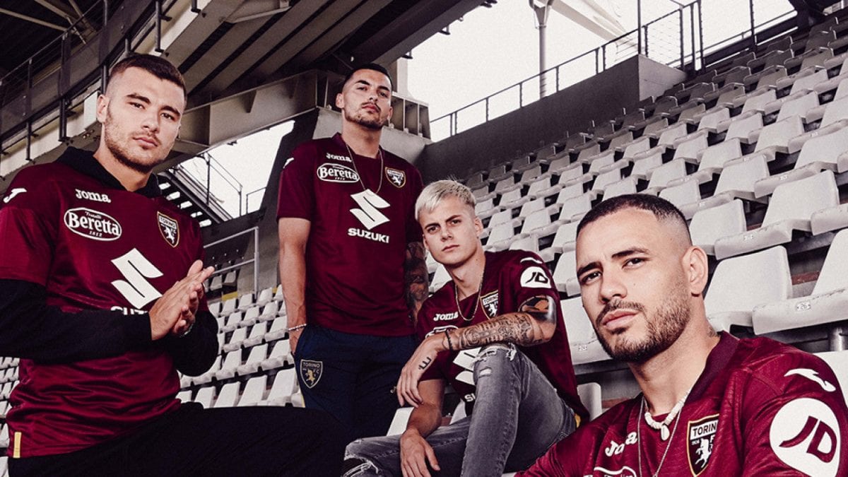 Four men in maroon Torino FC jerseys pose together on empty stadium seats, creating a team portrait in the stands.