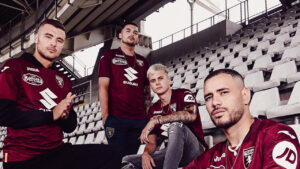 Four men in maroon Torino FC jerseys pose together on empty stadium seats, creating a team portrait in the stands.