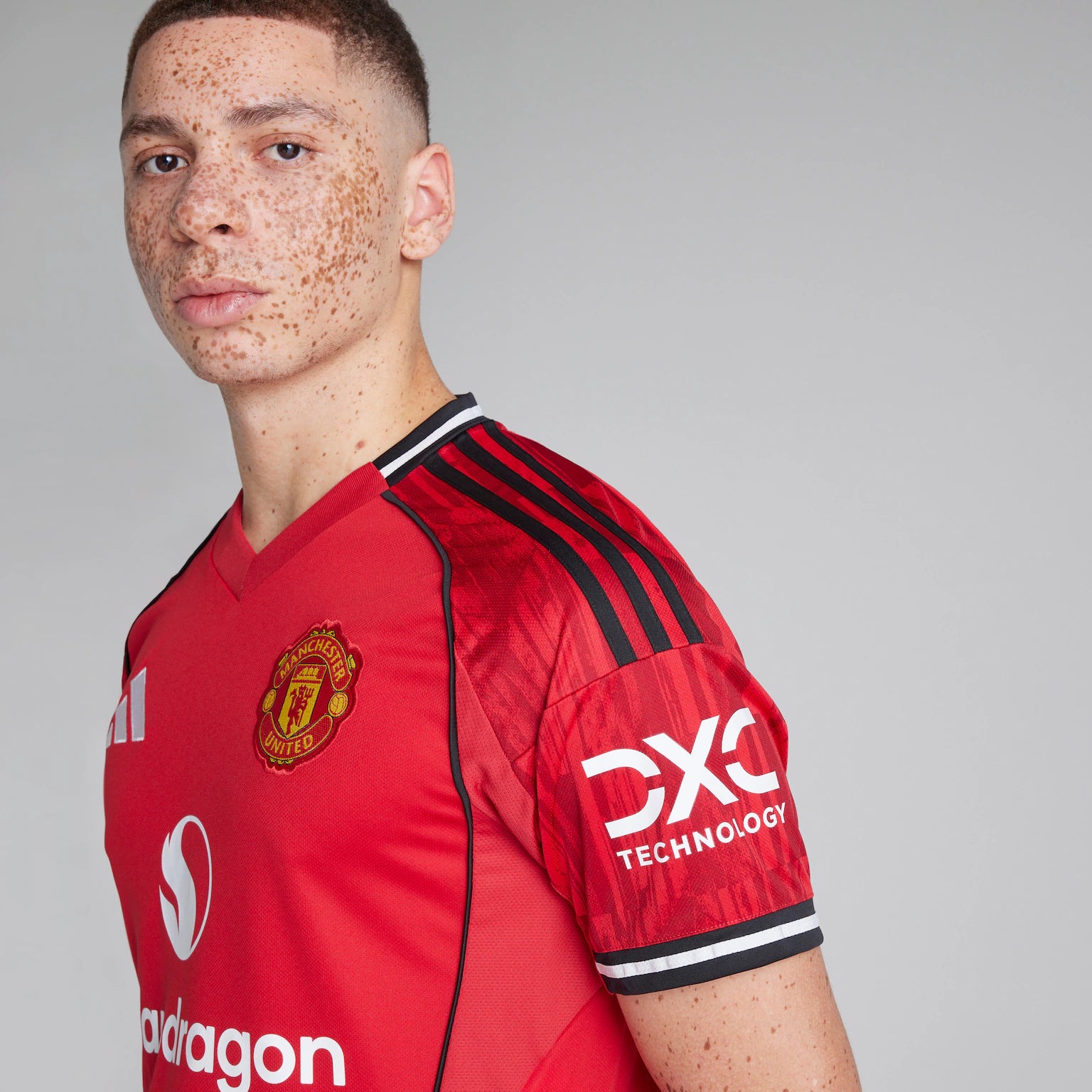 1a9140aa204004a4b6e82eece2a09a61 | UAE SPORT STORE Portrait of a person with freckles wearing a red Manchester United jersey, looking toward the camera against a neutral gray background, cropped at the shoulders.