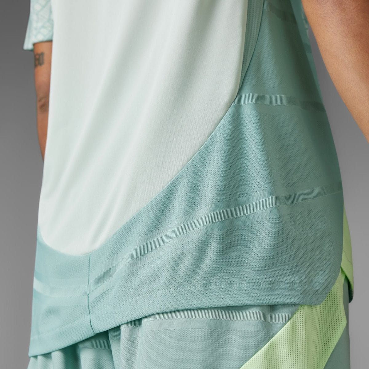 Close-up of layered mint-green athletic fabric with mesh panels and curved seams.