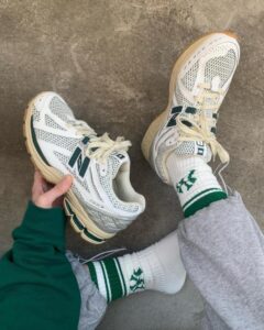 Top-down view of white and beige sneakers with green accents on a concrete floor, paired with white socks that have green stripes.