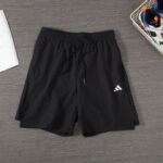Black athletic shorts with a drawstring lying on a wooden floor, Adidas logo visible on the left leg.