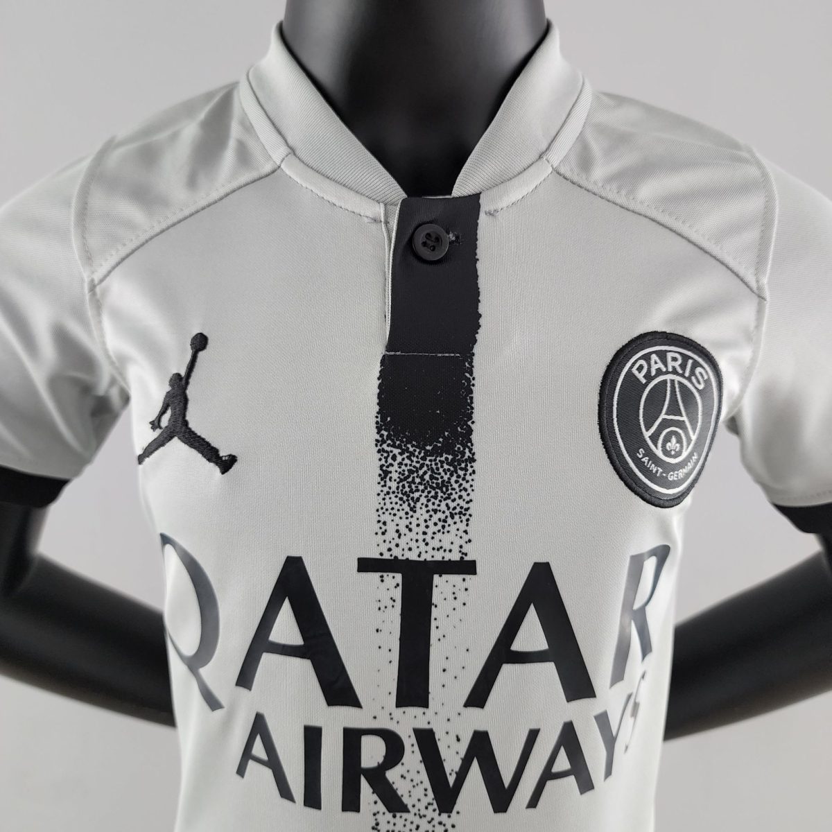 Close-up of a white jacket on a mannequin, with a black vertical stripe down the front and a circular Paris badge on the chest.