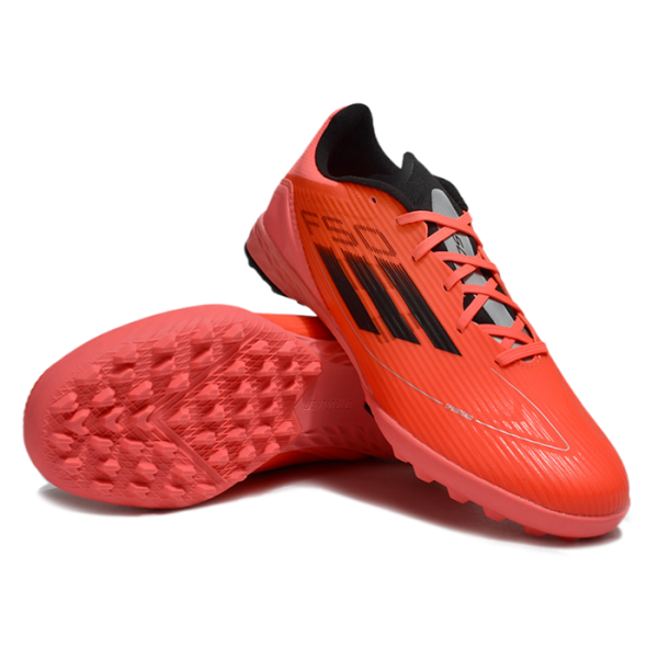 Orange Adidas soccer cleats with black stripes and pink laces, shown from the side with the outsole facing up to reveal traction studs.