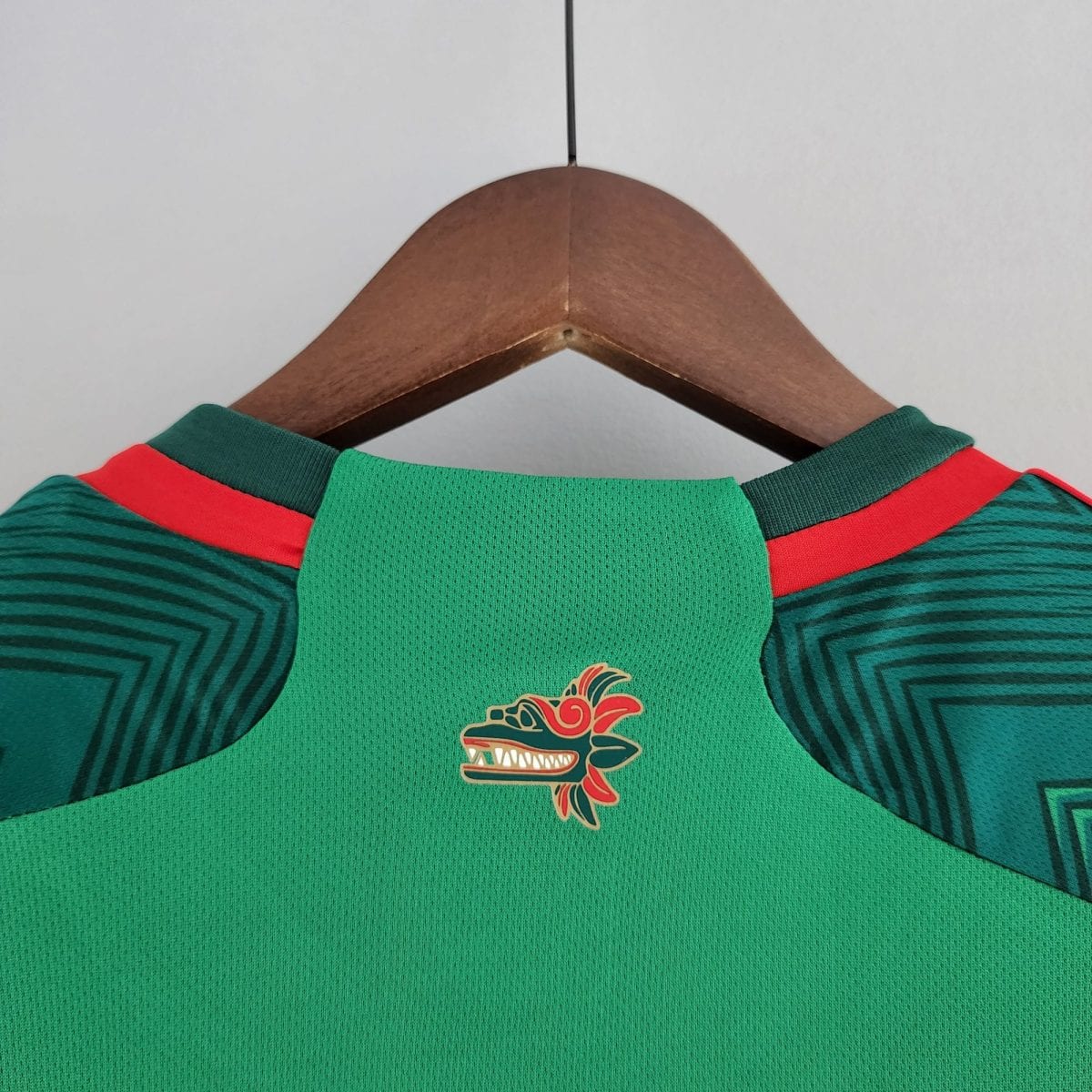 Green sports jersey on a wooden hanger with red shoulder stripes and a dragon emblem on the chest area.