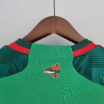 Green sports jersey on a wooden hanger with red shoulder stripes and a dragon emblem on the chest area.