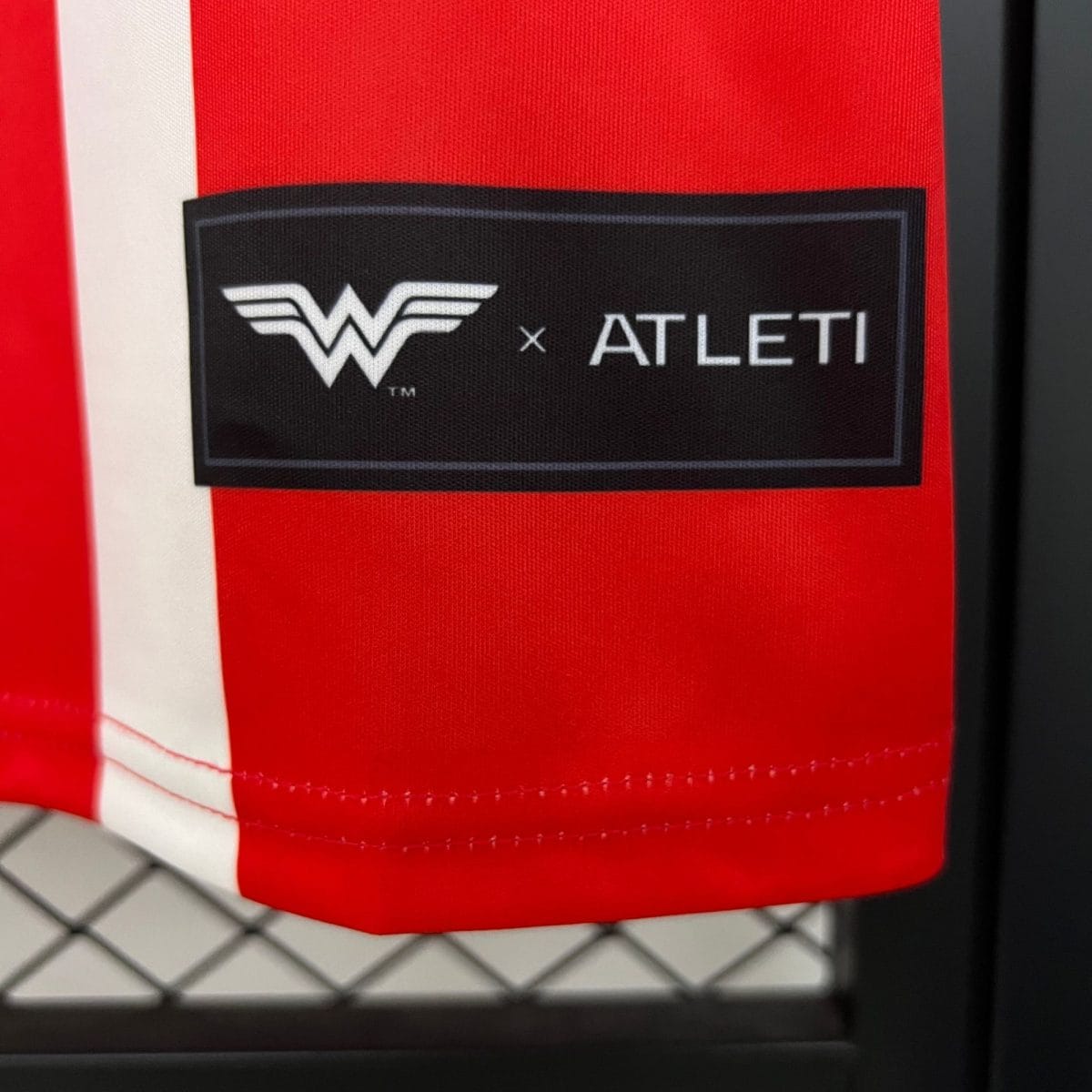 Close-up of red fabric with a black label showing a white logo and the text 'x ALT' against a fence background.