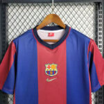 Blue and red FC Barcelona jersey hanging on a wooden hanger, featuring the club crest and Nike logo in the center.