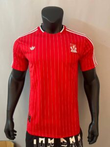 Red pinstriped Adidas football jersey with white shoulder stripes and a crest on the left chest, displayed on a black mannequin.
