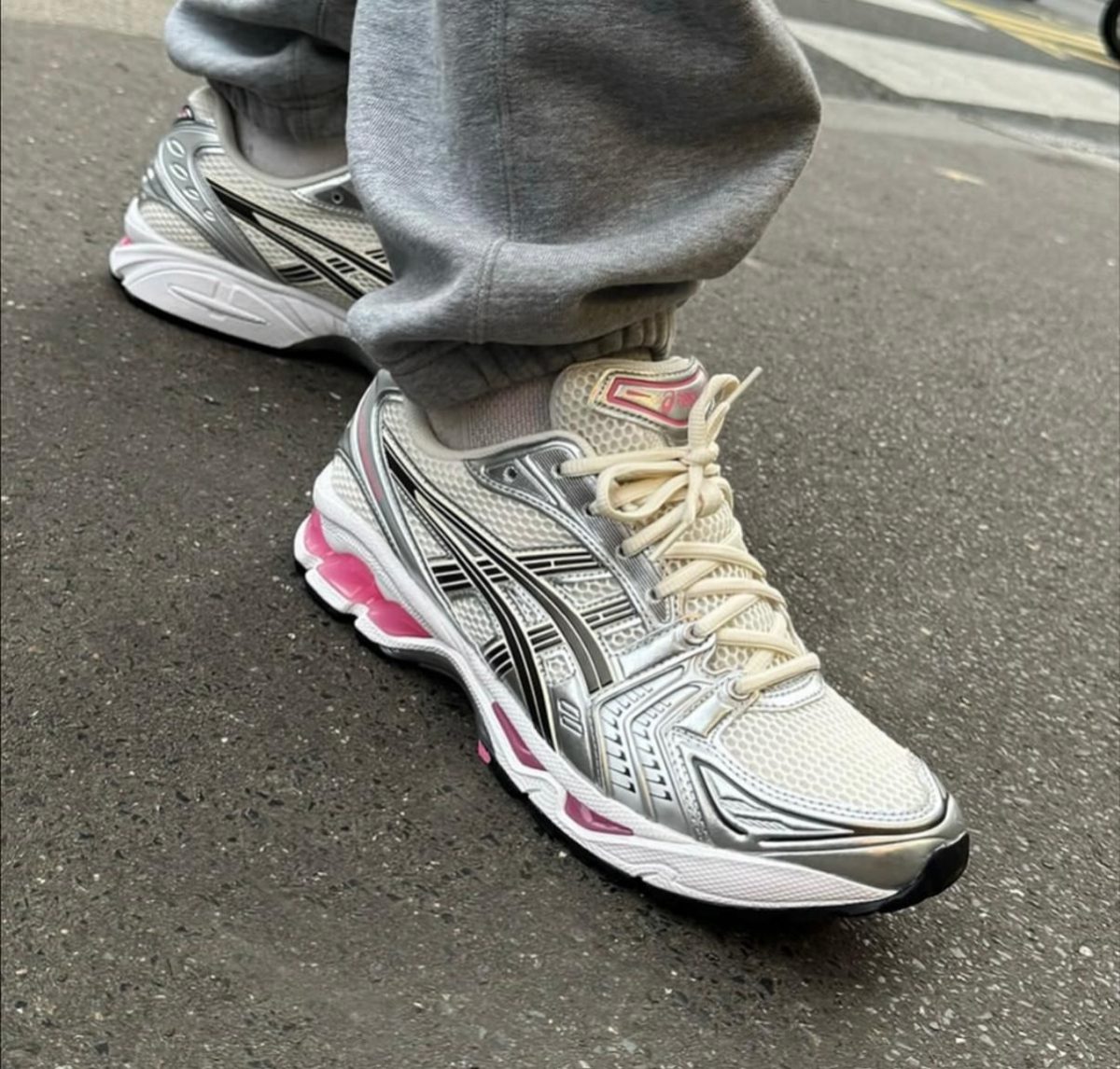 Close-up of a person wearing light gray sweatpants and silver-white running shoes with black stripes and pink accents, standing on a paved street.