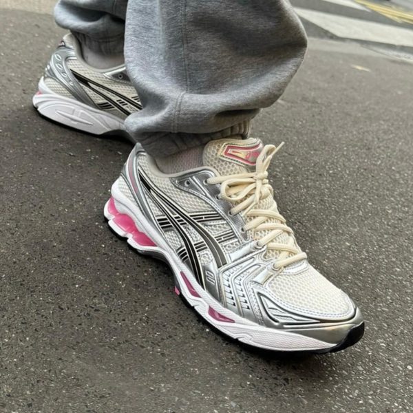 Close-up of a person wearing light gray sweatpants and silver-white running shoes with black stripes and pink accents, standing on a paved street.