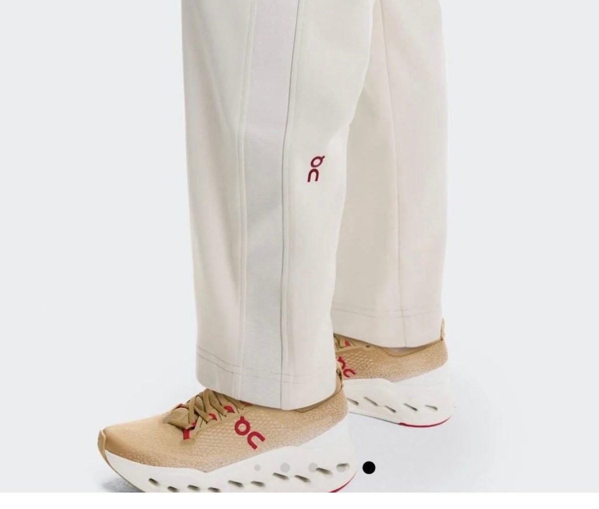 Beige athletic sneakers with red ON logo, paired with light beige pants showing a chunky white sole with cutouts.