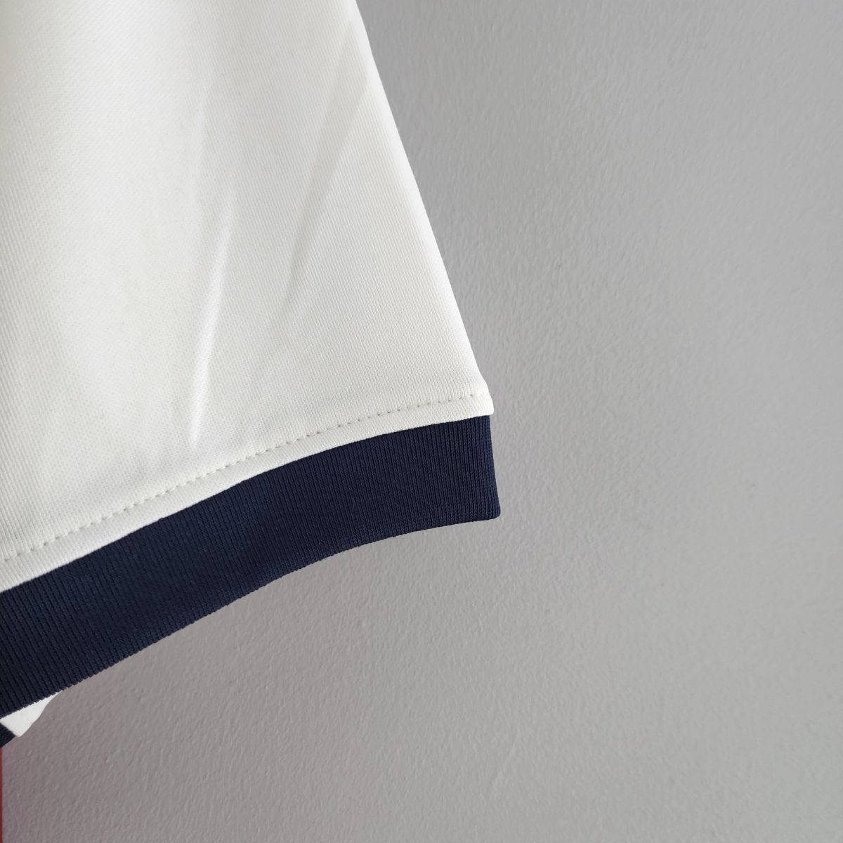 Close-up of white fabric with a navy blue striped edge, showing textured knit material and stitching detail on a gray background.