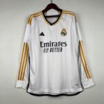 White Real Madrid football jersey hanging on a wooden hanger, with gold shoulder stripes and the club crest visible.