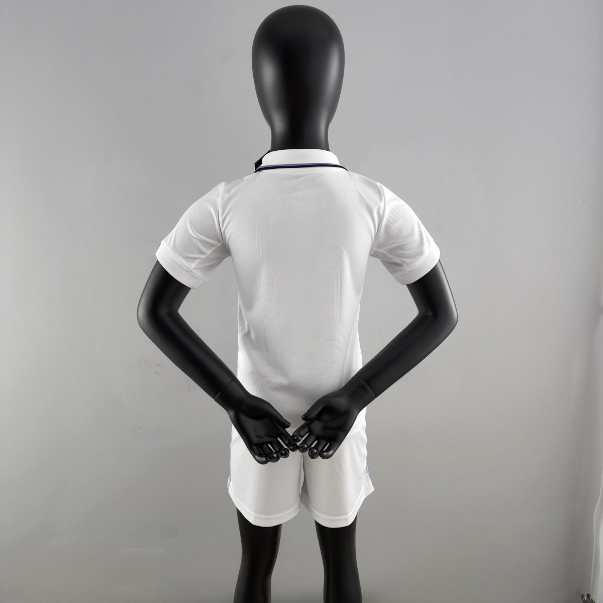 Back view of a black mannequin wearing a white shirt, arms bent with hands together in front against a gray backdrop.