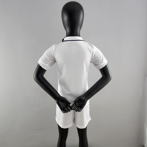 Back view of a black mannequin wearing a white shirt, arms bent with hands together in front against a gray backdrop.