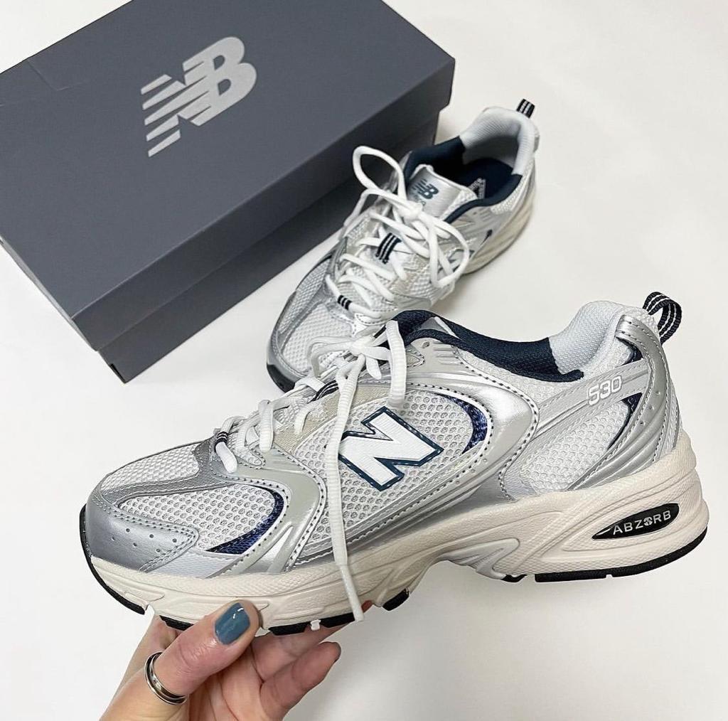 1f16314e-d0b2-4075-8030-51a3cbf07b3d | UAE SPORT STORE Silver and white New Balance 530 sneakers with blue accents, placed next to a gray NB box.
