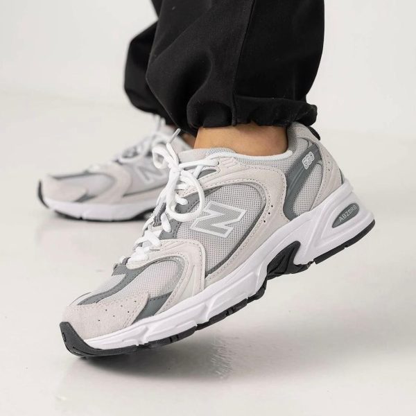 Grey and white New Balance running shoes on a person stepping forward, black joggers visible at the ankle.