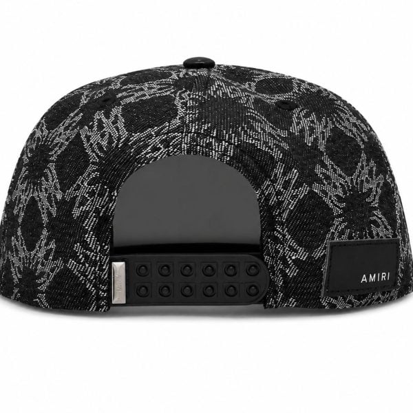 Back view of a black-and-white patterned snapback hat with an adjustable plastic strap and an AMIRI label patch on the side.