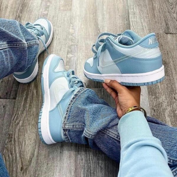 Person wearing light blue Nike sneakers sits on a wooden floor, holding one shoe in hand. You can see denim jeans and a bracelet on the wrist.