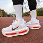 Pair of white Nike running shoes with visible red air-sole units, worn with tall white socks on a red running track.