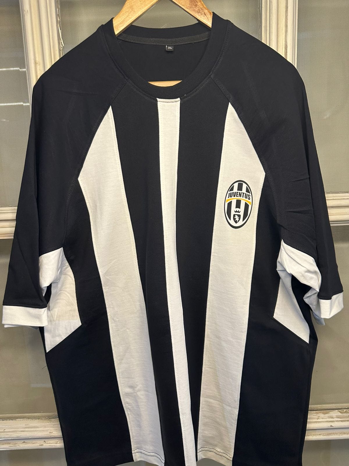 1f8d4627-e461-4052-bb63-069c1d15cebc | UAE SPORT STORE Juventus soccer jersey hanging on a wooden hanger with bold black and white vertical stripes and the team badge on the left chest area
