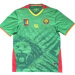 Green Cameroon national football jersey with red/yellow trim and crest on the left chest, lion emblem on the right.