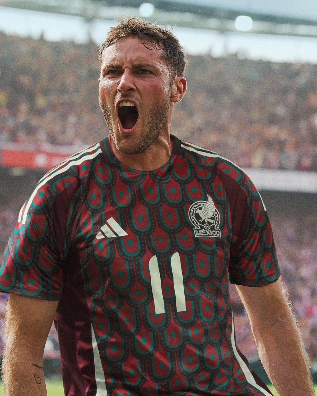 Male soccer player wearing Mexico national team jersey, shouting with mouth wide open during a game.