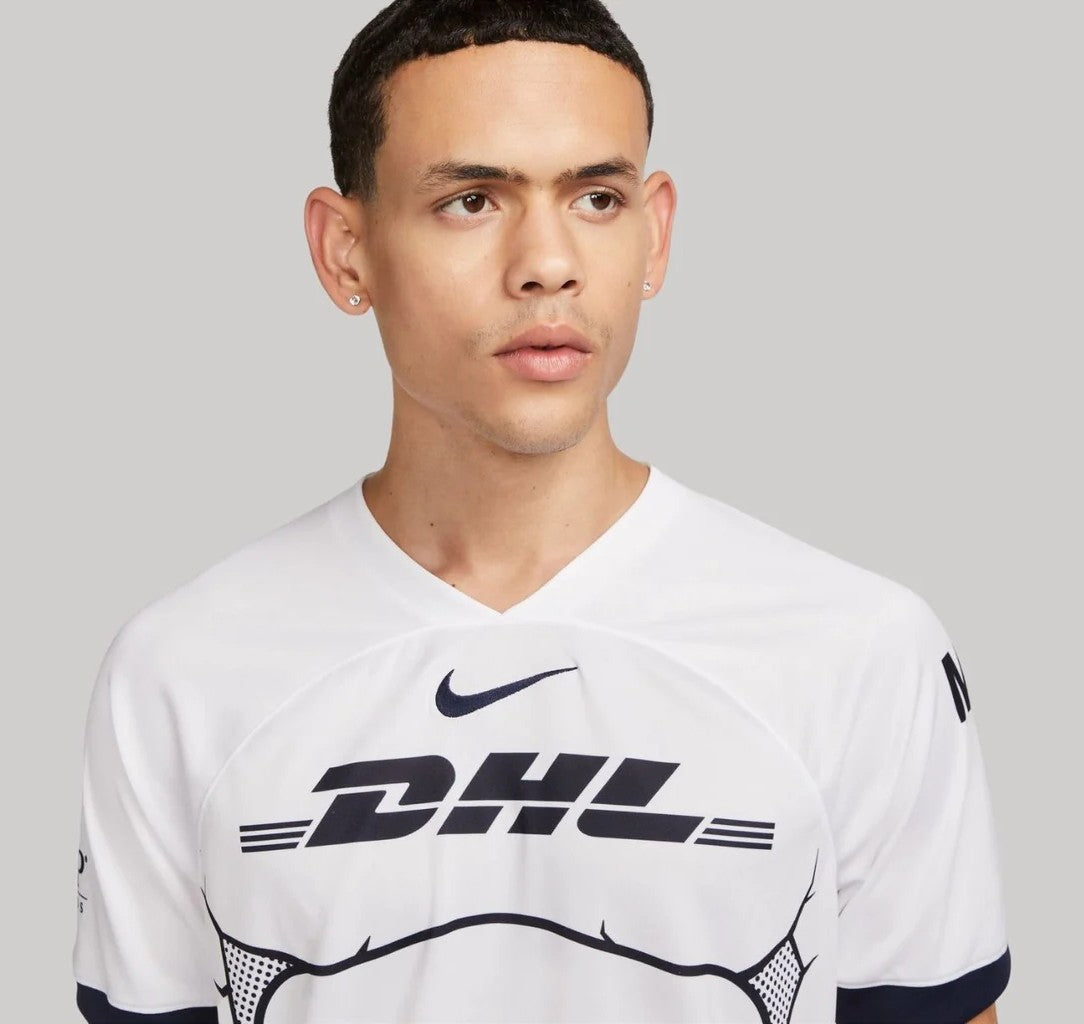 1xaugzAWFoi3YsS_6de6a8ea-314e-4ebf-ab63-bdd9b4187e8e | UAE SPORT STORE Portrait of a man wearing a white DHL jersey with a Nike logo, looking off to the side against a gray background.