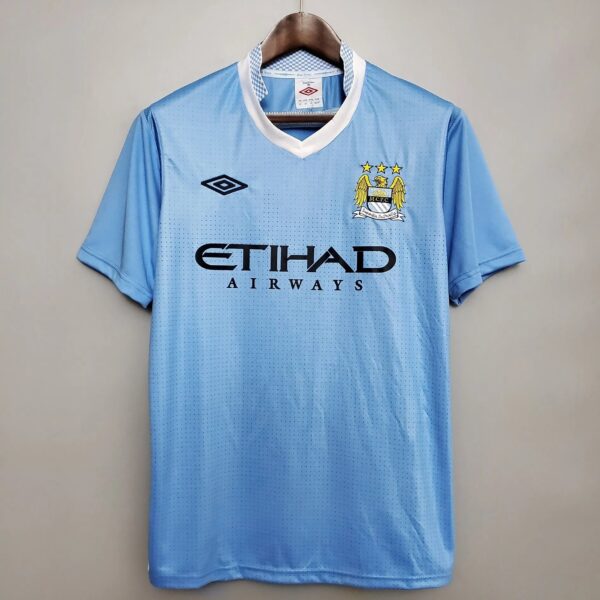 Light blue Manchester City jersey on a hanger, showing club crest with three stars and the ETIHAD AIRWAYS sponsor.