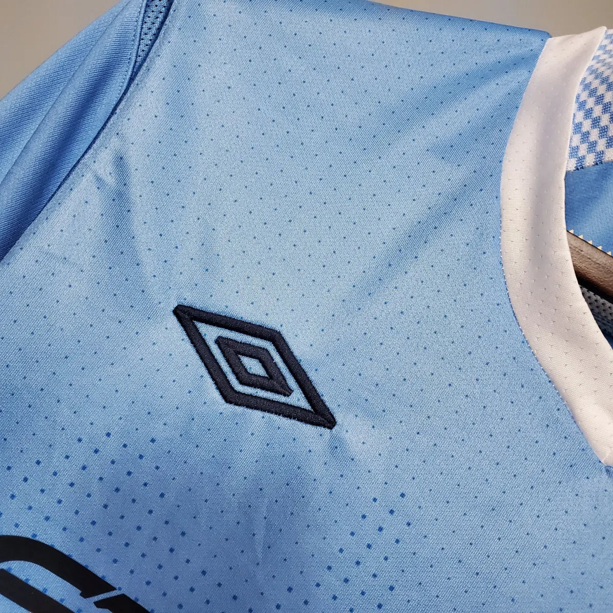 2012-Manchester-City-Retro-Home-Short-Sleeve-Jersey4 | UAE SPORT STORE Light blue sports jersey fabric with a dark blue double-diamond Umbro logo on the chest area.