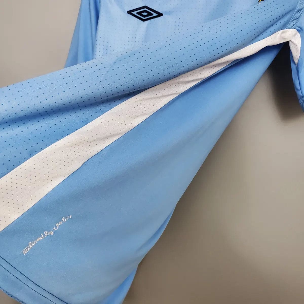 2012-Manchester-City-Retro-Home-Short-Sleeve-Jersey7 | UAE SPORT STORE Light blue perforated sports jersey sleeve with a white stripe and the Umbro diamond logo on the shoulder area.