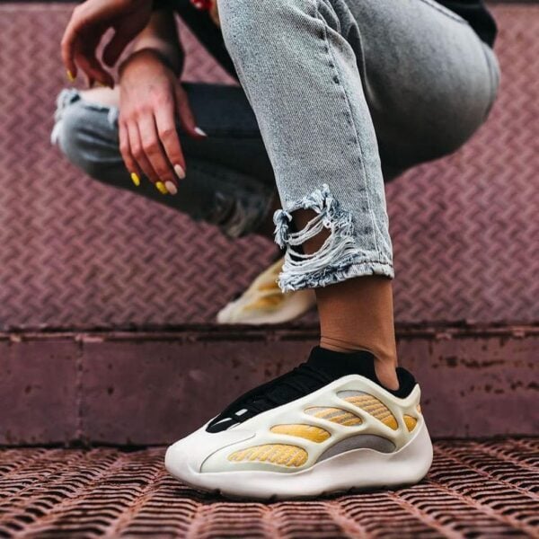 Close-up of a white and gold sneaker on a person wearing ripped jeans, crouching on a metal staircase.