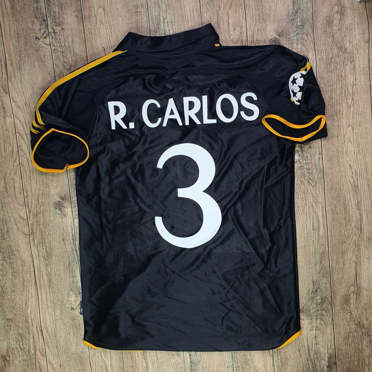 Black athletic jersey with yellow trim, displaying the name 'R. CARLOS' and number 3 on a wooden floor.