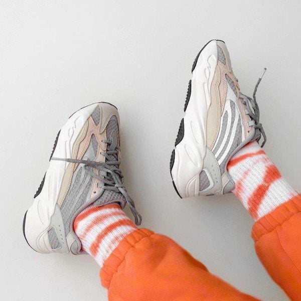 Gray and beige sneakers worn with orange and white striped socks, bright orange joggers visible at the ankles