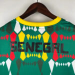 Green geometric-pattern shirt with a yellow collar, hanging on a wooden hanger; bold black 'GENERAL' across the back.