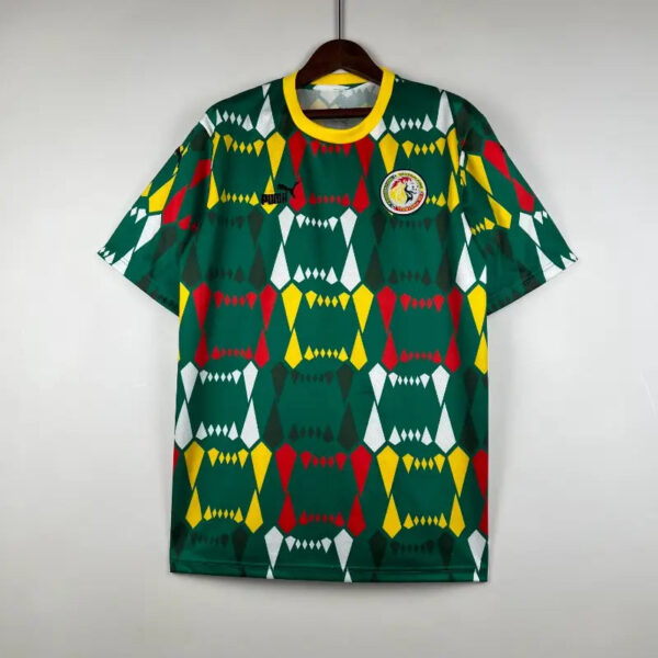 Green sports jersey with a bright yellow collar featuring a bold geometric pattern in red, yellow, white, and dark green; circular club badge on the chest.