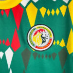 Close-up of a green soccer jersey with red, yellow, and gray geometric shapes and the Senegal Football Federation crest in the center.