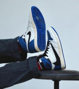 Pair of white and blue sneakers with black swoosh, feet resting on a chair, blue sole visible.