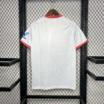 White soccer jersey hanging on a wooden hanger, red zigzag trim at the collar and sleeve cuffs against a metal mesh backdrop.