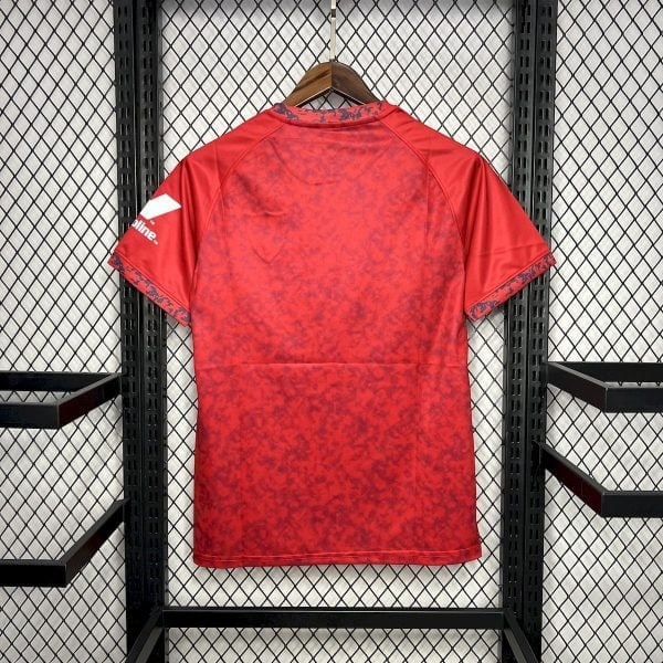 Red athletic jersey with a red camouflage pattern hangs on a wooden hanger against a black metal grid wall.