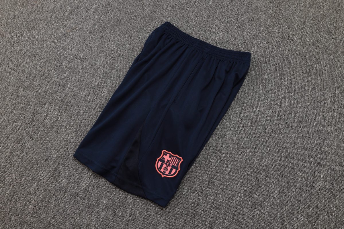 Navy athletic shorts with a pink FC Barcelona crest on the lower leg, laid on a gray carpeted floor.