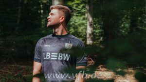 2048x1152_03_00000_fw_1152x648_32d2e018-40a8-4bb5-b505-91cda913c449 | UAE SPORT STORE Man in a dark soccer jersey stands in a sunlit forest, looking off to the left.