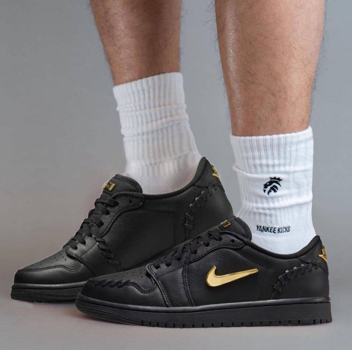 Lower legs in white ribbed crew socks with black sneakers featuring a gold Nike swoosh