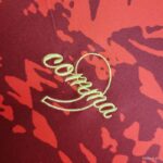 Embroidered green cursive text 'Cordoba' with a heart outline on red patterned fabric (decorative textile).
