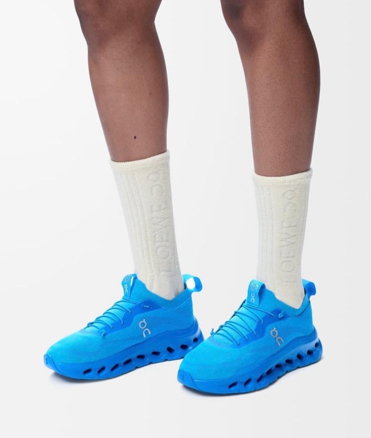 Bright blue On running sneakers worn with off-white crew socks, standing against a white background.