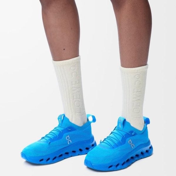 Bright blue On running sneakers worn with off-white crew socks, standing against a white background.