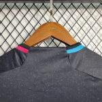 Back view of a dark gray speckled athletic shirt with pink and blue collar accents on a wooden hanger against a metal grid wall.